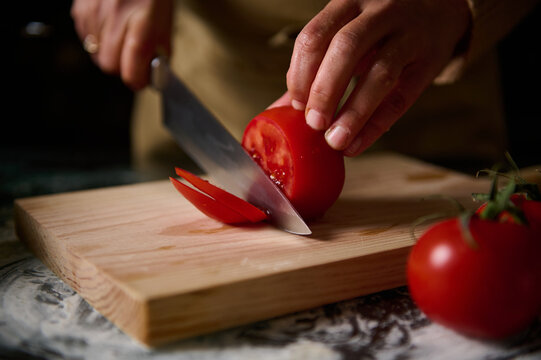 Close-up of hands slicing fresh tomato on wooden cutting board