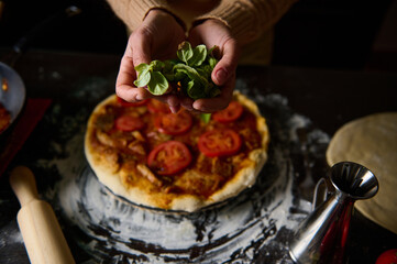 Hand adding fresh basil to homemade tomato pizza in kitchen