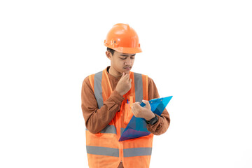 Young Indonesian male construction worker in full safety gear is seen thinking while filling out a report on a clipboard, construction and industry concept, isolated on white background.