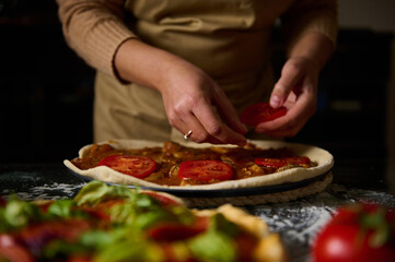 Person preparing homemade pizza with fresh tomato slices in a rustic kitchen