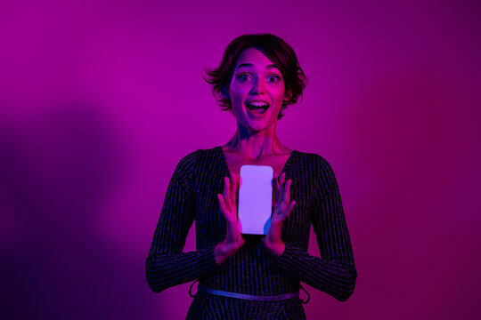 Photo portrait of attractive young woman hold excited white screen wear trendy overall clothes isolated on neon light pink color background