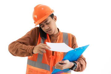 Young Indonesian male construction worker in full safety gear having trouble looking at report on clipboard while making voice call on mobile phone, construction concept, isolated on white 