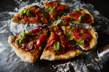 Sliced homemade pizza with fresh basil and tomato toppings on a floured surface