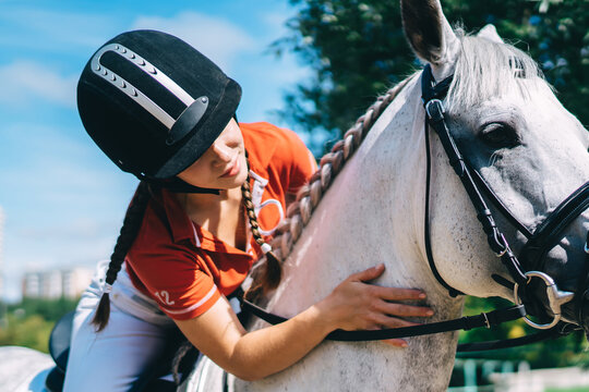 Young jockey woman hugging champion horse during summer walk for practicing riding skills during equestrian training outdoors, concept about love between people and animals - Focus on pet face