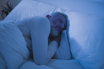 Elderly man peacefully sleeping in bed wearing comfortable pajamas during early morning