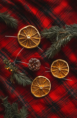 Dried orange slices and herbs on strings, laid out on red plaid fabric, with Christmas decorations in a boho style.