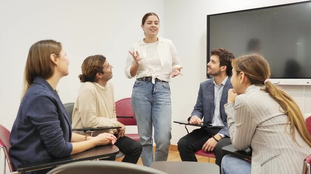 Young female professor explaining subject to classroom full of students