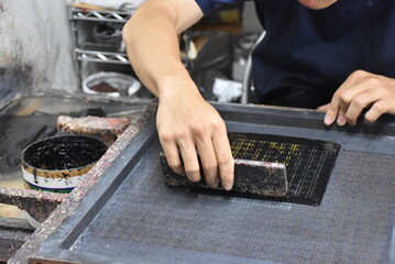 The intricate printing of a Japanese Inden pattern, as lacquer urushi is delicately applied onto soft deer leather, forming shimmering, textured designs under skilled hands.