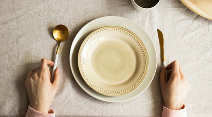 Female hands hold a fork and knife on a beige background with a plate, top view