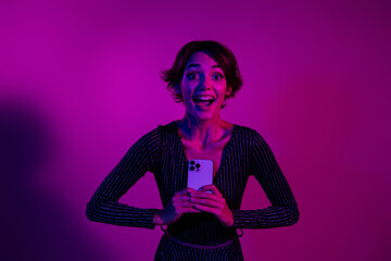 Photo portrait of attractive young woman hold excited gadget dressed stylish overall clothes isolated on neon light pink color background