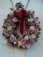 Elegant christmas wreath decorated pine cones on white light grey wooden door. Christmas mood. Beautiful vintage door. Christmas mood: festive christmasy themed winter natural wreath on a grey wooden 