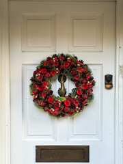 Elegant christmas wreath decorated pine cones, red flowers and fir trees on white light white wooden door. Christmas mood. Beautiful vintage door. Christmas mood: festive christmasy themed winter natu