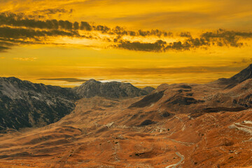 Naklejka premium Golden sunset over a majestic mountain landscape with dramatic sky and rocky terrain.