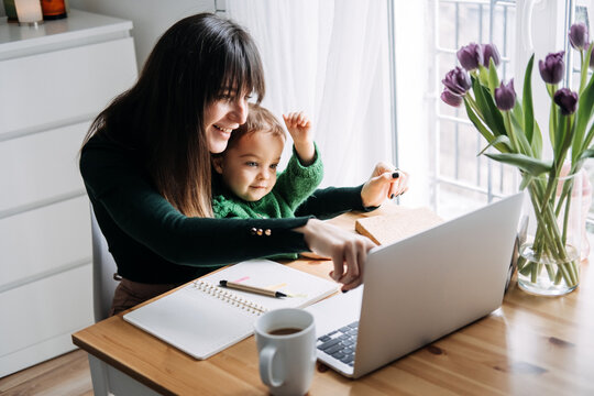 Mother working from home with curious toddler. Family-friendly work environment, home office setup, work-life integration, supportive parenting, multitasking
