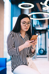 Young woman browsing cellphone in hall near entrance