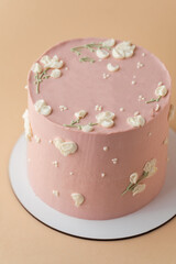Beautiful birthday cake with peach color chocolate icing on the beige pastel background decorated with cream flowers