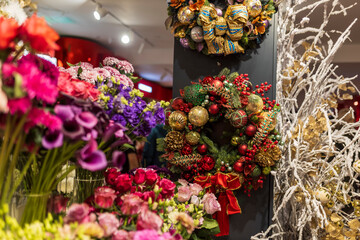 Wreath made of gold and red vintage glass Christmas ornaments, fir and spruce branches, dried grasses, gold-painted leaves, pine cones, and ribbons decorates the wall in a flower shop.