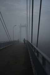 People are walking on a pedestrian bridge. Everything is in fog. Nothing is visible. Monochrome.