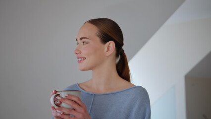 Peaceful woman drinking tea cup looking at camera in morning interior closeup