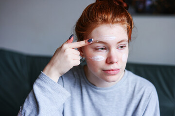 Girl caring of her beautiful skin on the face. Applying moisturizer on her face at home.