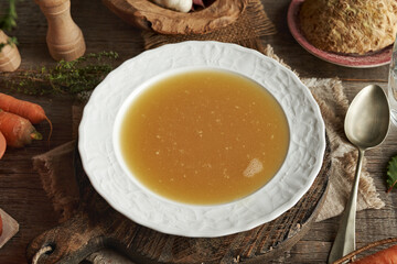 Chicken bone broth in white plate with fresh vegetables on a table