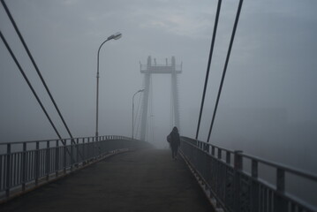 People are walking on a pedestrian bridge. Everything is in fog. Nothing is visible. Monochrome.