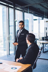 Group of successful male and female corporate experts collaborating near office desk with laptop and documents, diverse executive managers discussing together business briefing for sharing experience