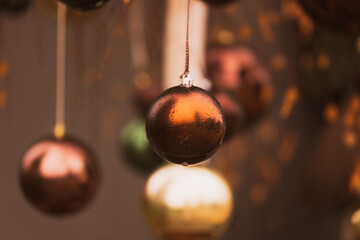 A close-up view of elegant Christmas baubles in warm metallic tones hanging delicately. The main...
