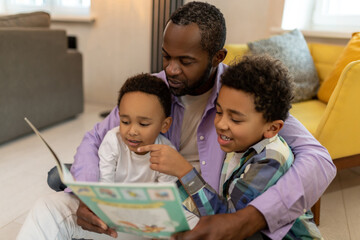 Dad and sons reading a book together and looking interested