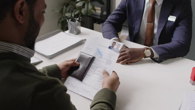 Over shoulder shot of bearded Indian man getting visa approved and happily shaking hand of Black male consular officer during interview in embassy