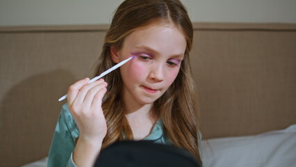 Funny toddler using makeup painting face with shadows. Little kid playing alone