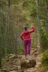Fototapeta premium A woman in a red jacket stands on a rock in a forest