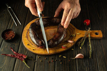 Hands expertly slice a dark, flavorful sausage on a wooden cutting board. Surrounding ingredients...