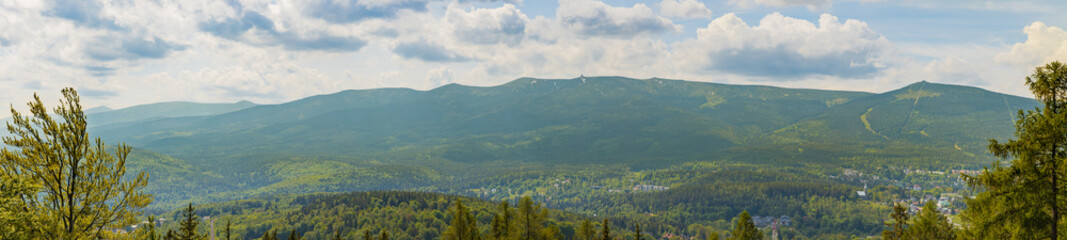Beautiful panoramic landscape of high mountains covered with green trees and bushes with small cities below at cloudy morning