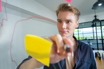 Professional caucasian businessman writing marketing idea by using mind map and sticky notes on glass board at modern meeting room. Creative business and planing concept. Closeup. Immaculate.