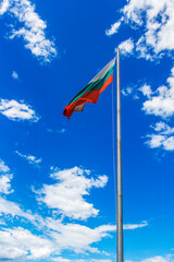 Bulgarian national flag on a metal pole against sunny sky with clouds
