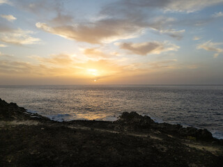 Atlantic ocean sunset in Tenerife with soft golden hues illuminating the horizon, waves gently crashing against the rocky shore.  A scene that evokes a sense of tranquility and connection with nature