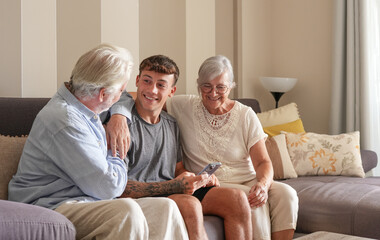 Fototapeta premium Happy multigenerational family of white-haired grandparents and young grandson sitting together on sofa at home. The old and new generation share pleasant moments in harmony