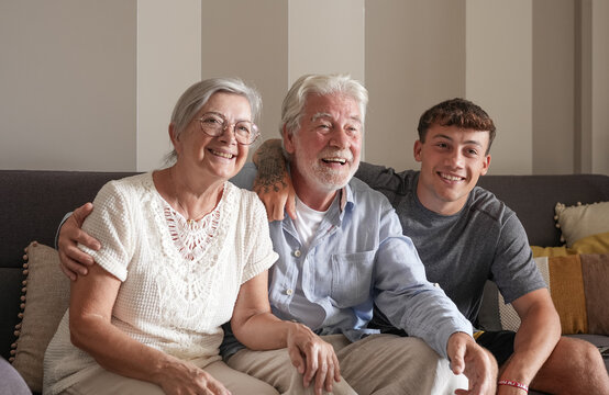 Happy multigenerational family of white-haired grandparents and young grandson looking at tv entrainement sitting together at home. Three generations of caucasian family