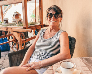 Happy smiling elderly woman relaxing at cafe table enjoying a coffee break, mature lady in...