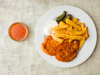 Breaded chicken fillet meal and fried potatoes chips with ridges on a white plate and light color table cloth. Simple food made of high quality premium products. Cooked poultry meat.