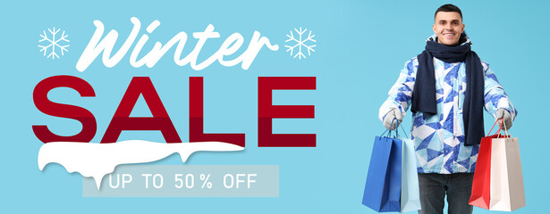 Young man in stylish puffer jacket and scarf with shopping bags on blue background