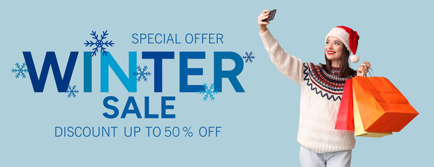 Young woman in Santa hat taking selfie with shopping bags on blue background