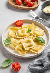 Homemade ravioli pasta with cheese, tomatoes and basil in a plate on a light  background with  fork and napkin.