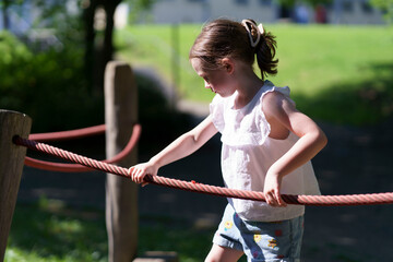Little cute girl without front tooth rope playground summer park. Concept of active healthy...