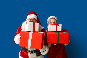 Santa Claus and beautiful young woman with Christmas gifts on blue background