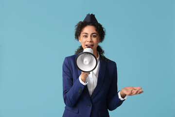 Beautiful African-American stewardess with megaphone on blue background