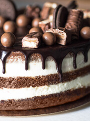 Close-up of a chocolate cake with creamy layers, covered with dripping chocolate frosting, chocolate candies and bars