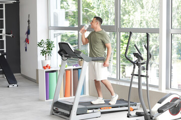 Sporty young man with bottle of water training on treadmill in gym