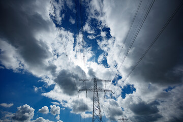 High-voltage power lines crisscross a partly cloudy sky, with a metal pylon prominent in the center.  A mix of bright and dark clouds.